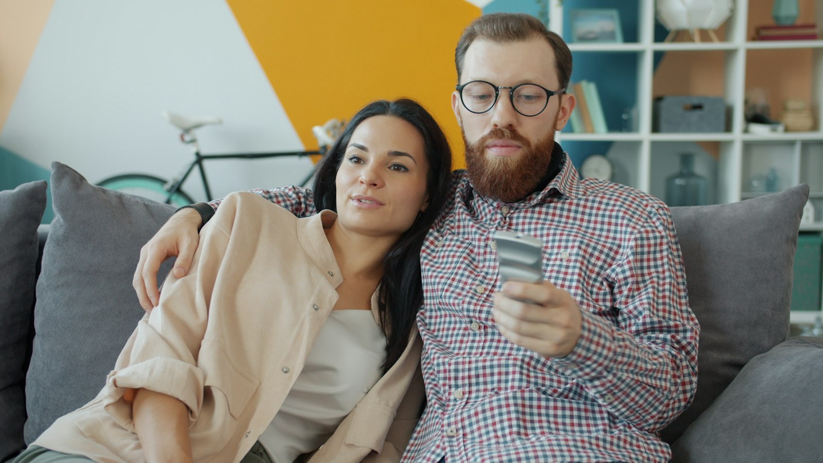 A couple relaxing on a sofa at home while one of them checks his phone